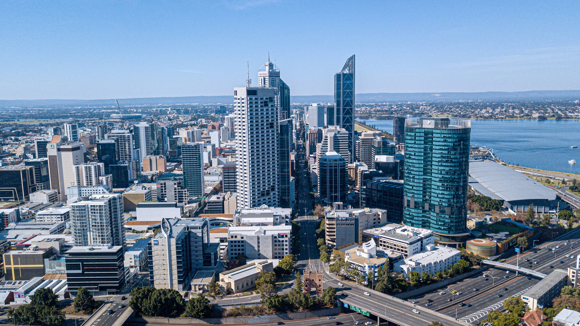 High-angle cityscape view of the Perth skyline featuring modern glass skyscrapers, including Brookfield Place and 108 St Georges Terrace, under a blue sky