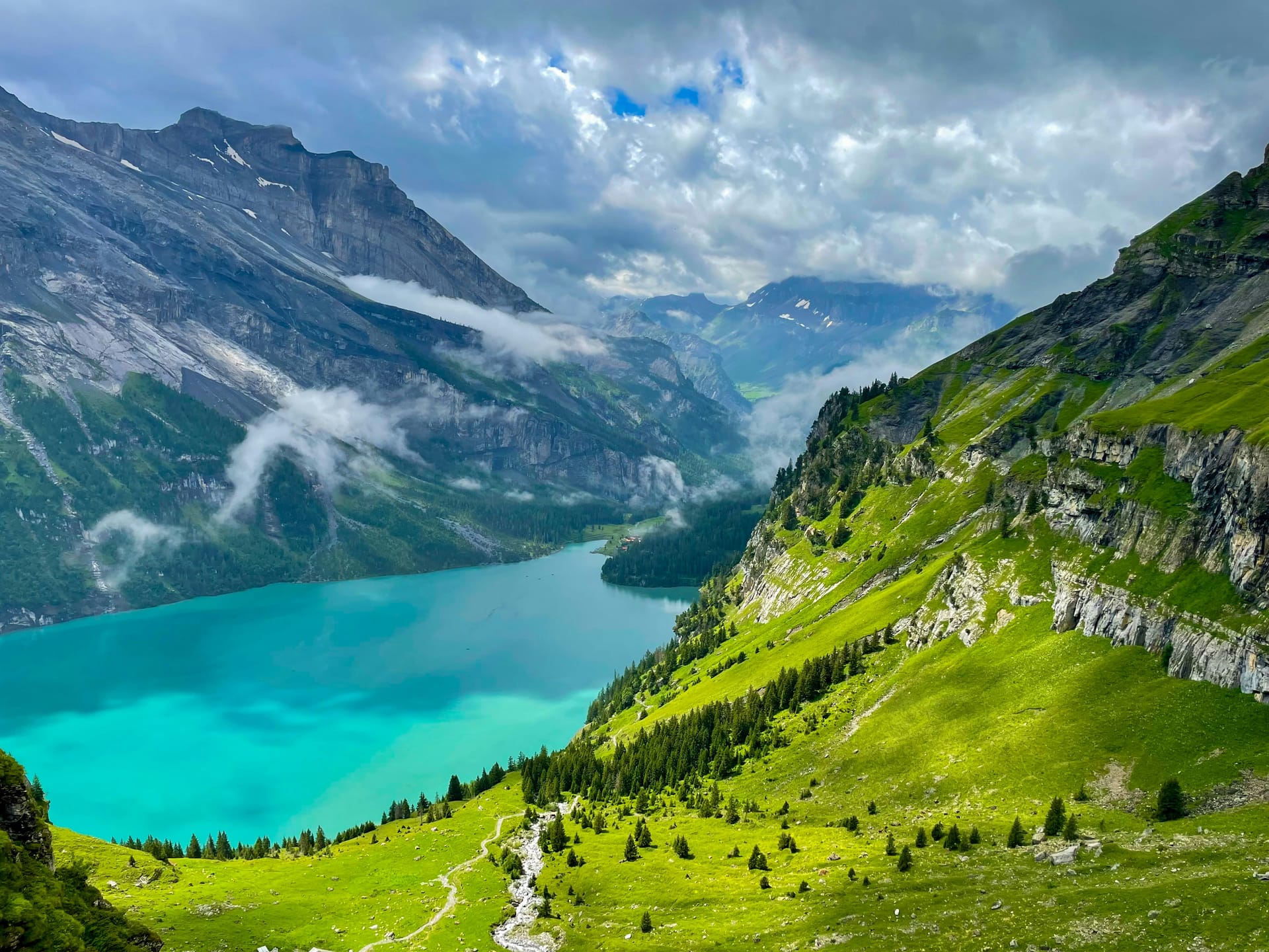 A vibrant turquoise alpine lake surrounded by steep green mountain slopes and gray rocky cliffs.