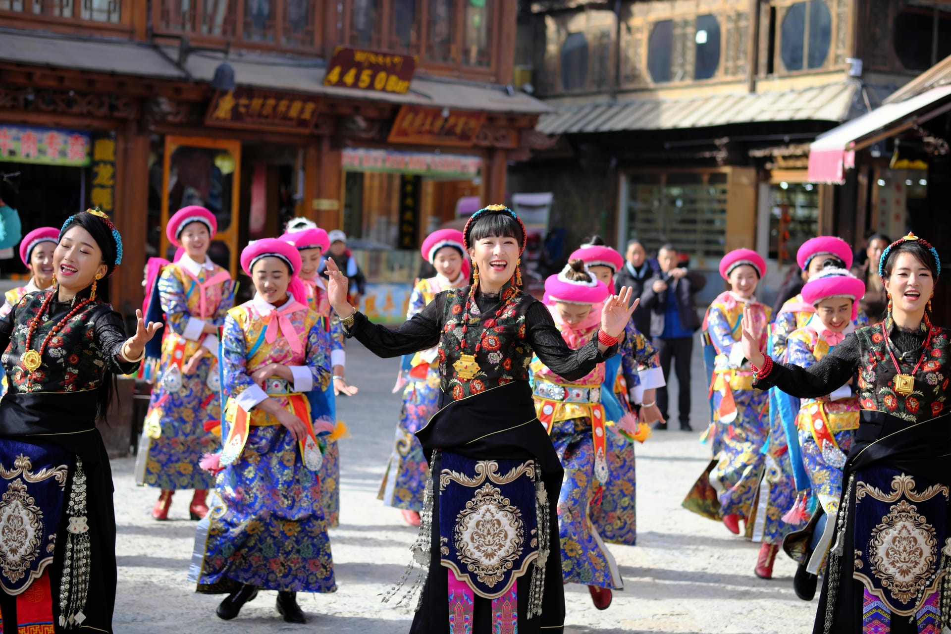 Women wearing traditional Yunnan ethnic minority clothing with bright pink hats dancing in a public square.