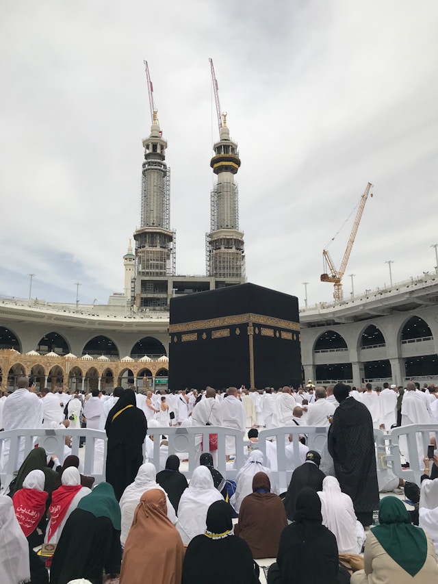 A view of the Kaaba surrounded by a large crowd of pilgrims in the courtyard of the Grand Mosque, with construction cranes visible in the distance